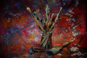 old brushes in a glas in front of colorful paper