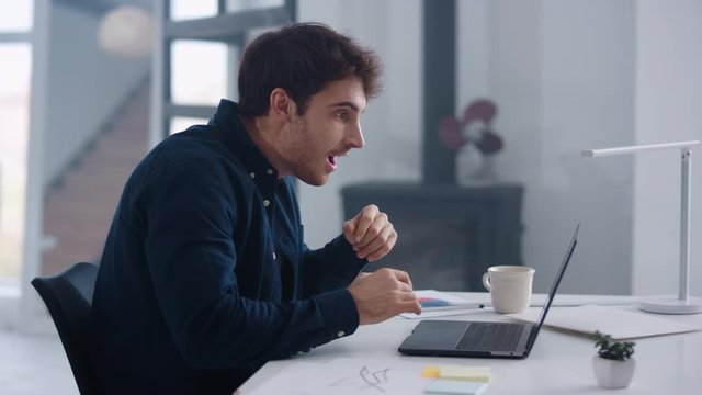 Happy business man working on laptop computer in office. Guy winning project