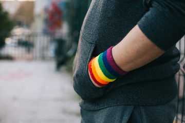 Side view of a boy with a gay pride bracelet with his hands in his pocket is standing on the street