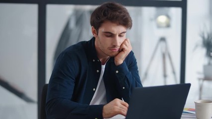 Boring business man looking computer screen in office. Tired guy working laptop