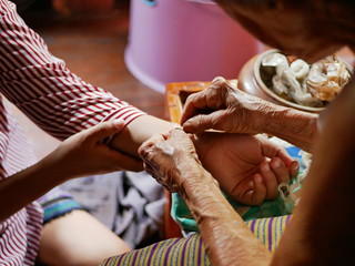 Hand of old woman waving a white string ( Sai Sin ) around her granddaughter hands - Thai...