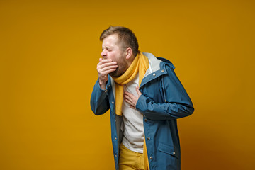 Man in a scarf and jacket coughs, covers mouth with palm and experiences pain. Copy space. Concept...