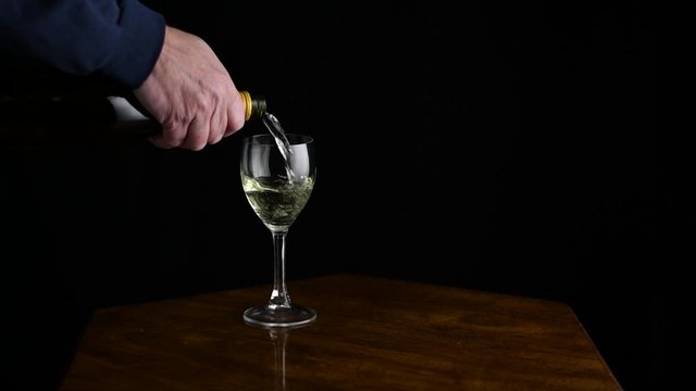 A mans hand pours a glass of wine, and then drops two pills into it. Pills drop in slow motion. He stirs the glass with his finger and picks it up. Dark scene on a black background.