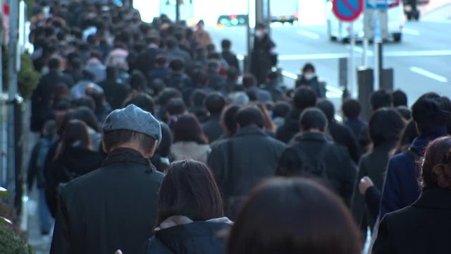 TOKYO, JAPAN - MARCH 2020 : View of crowd of people walking down the street in busy morning rush hour. Many commuters going to work. Japanese business, job and lifestyle concept. Slow motion shot.