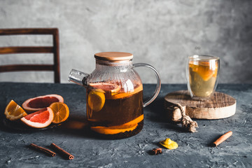 Citrus tea in a transparent teapot on a gray concrete background. Healthy drink, vegan, eco product.