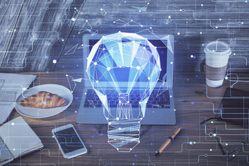 Computer on desktop in office with bulb icon hologram. Multi exposure. Concept of idea.