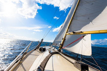 Sloop rigged yacht sailing on a clear day. A view from the deck to the bow and sails. Waves and...