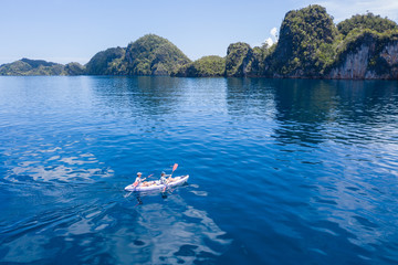 Kayakers cruise over blue seas and explore the amazing limestone islands that rise from Raja Ampat's seascape. This tropical Indonesian region is known for its incredible marine biodiversity.