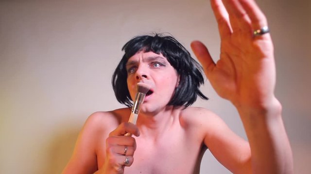 A man in a wig and with painted eyes sings in a makeup brush. The concept of fun moments of human life.