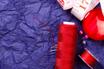 Flat lay. Round red buttons for clothes, a spool of thread and a tape measure on a crumpled purple...