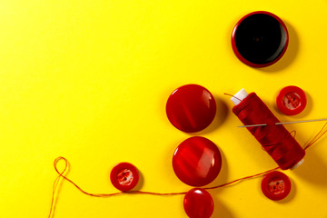 Flat lay. Background of items for sewing. Red buttons for clothes and a spool of red thread with a corner on a yellow background. Close-up, horizontal, top view, free space on the left. Hobby concept.