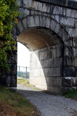 sun shining through grey stone brick tunnel with ivy growing up the wall 