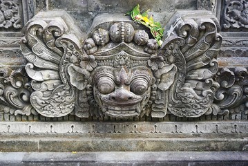 Ornate Balinese stone carving face with bulging eyes and sharp teeth at a temple in Bali Indonesia