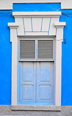 Naklejka premium Tall classic ornamental closed window with shutters in a blue wall.