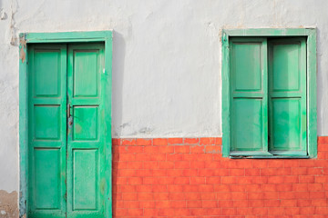 A green door and a green window in a wall with red bricks.