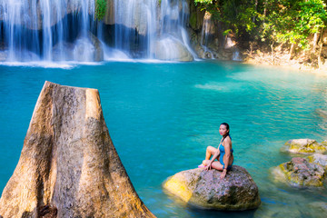 Woman in blue swimsuit sit enjoy at Erawan Waterfall and natural