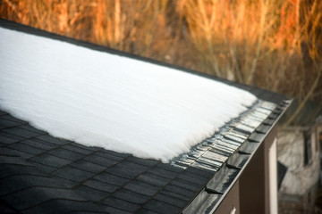 Snow melting on shingled roof with eavestrough drain in morning sun