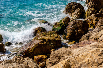 A close-up shot of the Mediterranean Sea turquoise water and powerful waves beating against the rocks on the coast