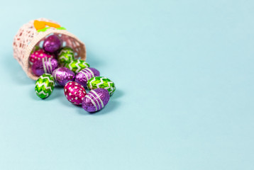 Colorful chocolate easter eggs in basket blue background. Small Chocolate eggs in a foil. Traditional Easter sweet. Copy Space