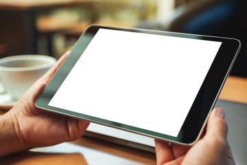 Mockup image of a woman holding black tablet pc with blank white screen with laptop and coffee cup on wooden table