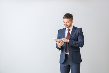 Handsome businessman with tablet computer on light background