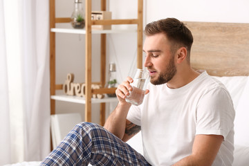 Morning of young man drinking water in bedroom