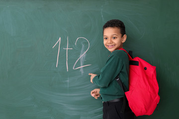 Cute African-American schoolboy near blackboard in classroom