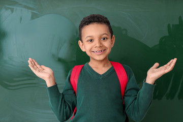 Cute African-American schoolboy near blackboard in classroom