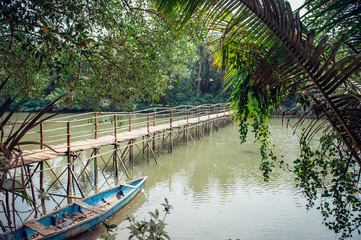 Old wooden bridge over a small river or pond, close up. Pedestrian bridge over the river on the background of green trees.