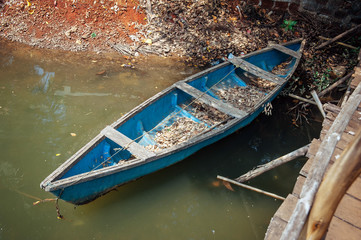 Obraz premium Old wooden boat in the water, top view. Small blue fishing boat on the bank of asian river, close up.