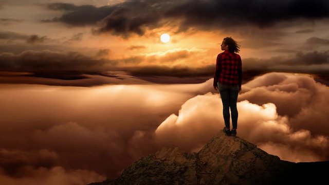 Girl on a Rocky Mountain Peak with Beautiful and striking view of the puffy clouds during a colorful and vibrant sunset or sunrise. Nature Background. Still Image Continuous Animation Cinemagraph