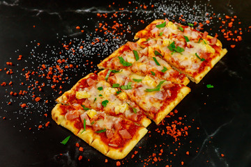 Slices of pizza with ham and pineapple topping on black background.
