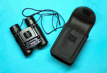 Binoculars. Binoculars with a case top view on a blue background close-up. Binoculars for hunting and observation. Augmentative. The concept of observation. Hiking binoculars for bird watching.