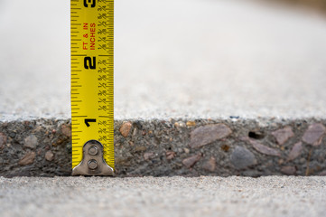 Frost heave crack in residential concrete sidewalk with tape measure 
