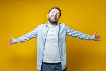 Beautiful, happy man stands with open arms, smiles and looks at the camera, on a yellow background.