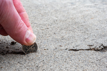 Stress crack in concrete slab with dime held by thumb and forefinger to test width