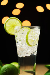 Glass of sparkling water soda drink lemonade with ice and lime lemon and leaf isolate on dark background.