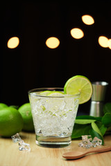 Glass of sparkling water soda drink lemonade with ice and lime lemon and leaf isolate on dark background.