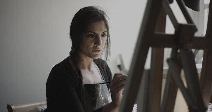 Young woman artist paints on canvas in her studio