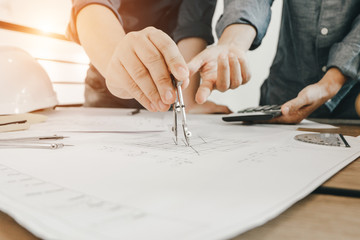 engineers pointing to building on blueprint and using laptop to drawing design building Project in office, construction concept. Engineer concept