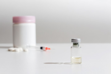 Liquid coronavirus COVID-19 vaccine is ready for use. Virus vaccine ampoule with syringe and tablets in background. Medicine and drug concept.