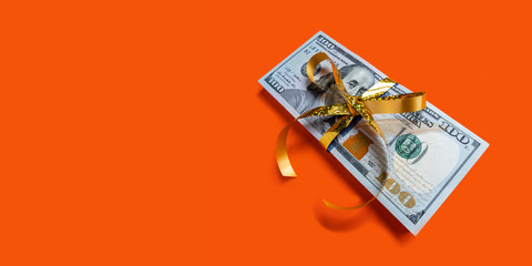 Stack of dollar banknotes with golden bow on orange background. Banner with copyspace concept