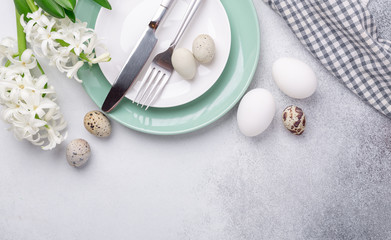 Fototapeta premium Beautiful Easter table setting in Scandinavian style. Green mint plate, eggs and silver cutlery on modern concrete background with hyacinth. Copy space. Top view