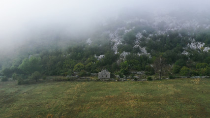 Aerial view of stone house without roof in mountains of Montenegro. Ruins, forest, fog, clouds. Grahovo