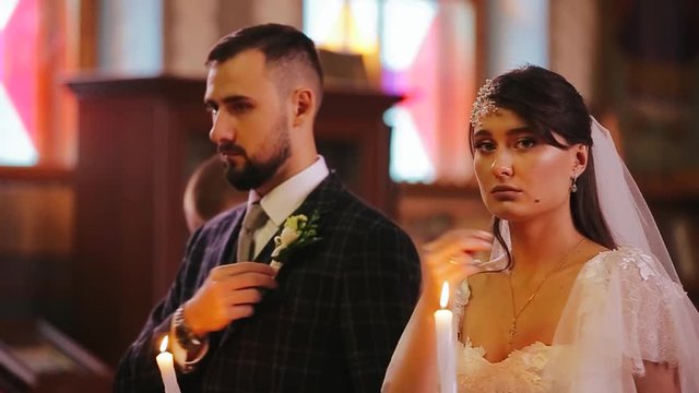 Stylish and beautiful wedding couple bride and groom holding candles and are baptized at a wedding ceremony in a Christian church. Close-up view of a beautiful bride in a dress and a man in a suit.