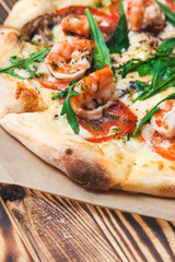 delicious classic Italian pizza with royal prawns and arugula on a wooden table close-up