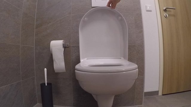 white faience toilet in the toilet room, girl closes the lid with her hand, the concept of germs, cleanliness, health