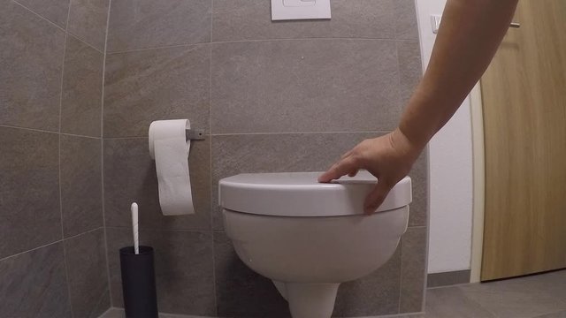 white faience toilet in the toilet room, girl closes the lid with her hand, the concept of germs, cleanliness, health