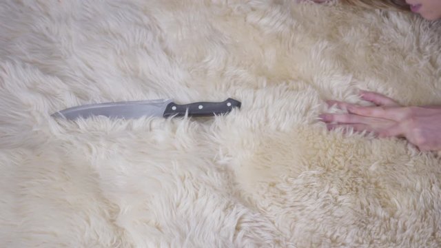 Young Caucasian woman trying to reach knife lying on soft carpet as senior unrecognizable man raping her. Concept of sexual violence, social problems.