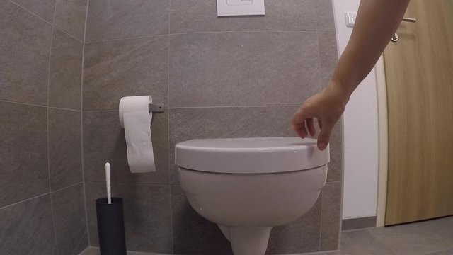 white faience toilet in the toilet room, girl closes the lid with her hand, the concept of germs, cleanliness, health